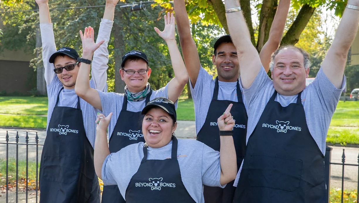 Bakers from Beyond Bones pose together celebrating with their hands in the air.